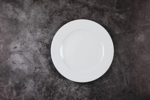 A white dinner plate on a grey and white marble surface