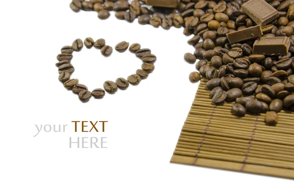 Granos de café negros en una estera de bambú y el corazón de los granos —  Fotos de Stock