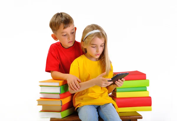 Two children read e-book surrounded by several books isolate on white background — Stock Photo, Image