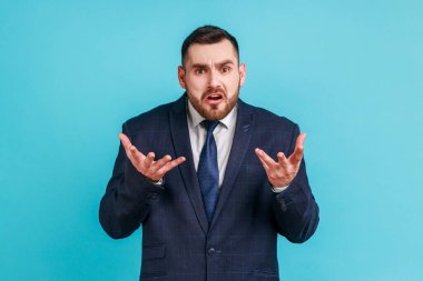 Nasıl yapabildin? Resmi stil takım elbise giyen sinirli sakallı adamın resmi portresi kaldırılmış eller ve kızgın bir yüzle neden diye soruyor. Mavi arka planda kapalı stüdyo çekimi.