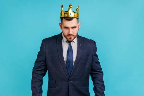 公式スタイルのスーツと黄金の冠の厳格な上司の男は 傲慢と怒り 特権的な地位を探して トップマネージャーや上司の位置にある 青い背景に隔離された屋内スタジオショット — ストック写真
