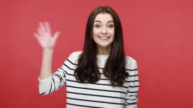 El sallayan kadın portresi, selam veren jest, güler yüzlü arkadaş canlısı, misafirleri selamlayan, gündelik tarzda uzun kollu gömlek giyen. Kırmızı arkaplanda kapalı stüdyo çekimleri.