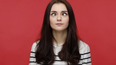 Woman looking cross eyed with stupid dumb face, girl having awkward confused comical expression, wearing casual style long sleeve shirt. Indoor studio shot isolated on red background.