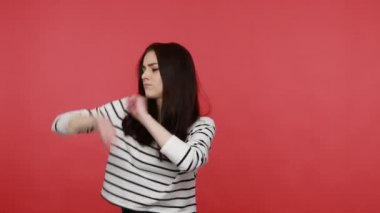 Dans eden kadın dans ederek poz veriyor, başarıyı kutluyor, zafer jestleri yapıyor, günlük tarz uzun kollu gömlek giyiyor. Kırmızı arkaplanda kapalı stüdyo çekimleri.