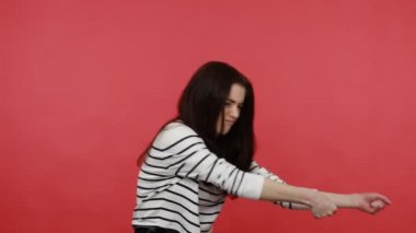 Güçlü esmer kadının portresi başarı elde etmek için büyük çaba sarf ediyor, halat çekiyor gibi yapıyor, gündelik tarzda uzun kollu gömlek giyiyor. Kırmızı arkaplanda kapalı stüdyo çekimleri.