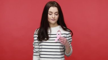 Pembe kurdele gösteren bir kadın, göğüs kanseri farkındalığının sembolü, kadın sağlığı ve hastalık önleme, günlük tarz uzun kollu gömlek giyiyor. Kırmızı arkaplanda kapalı stüdyo çekimleri.
