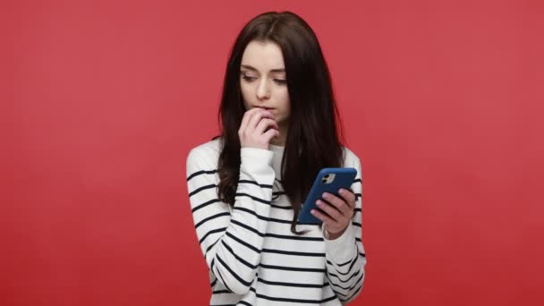 女性在智能手机上打字 表情周到 上网工作 做笔记 穿着休闲装长袖衬衫的肖像 在红色背景下隔离的室内拍摄 — 图库视频影像