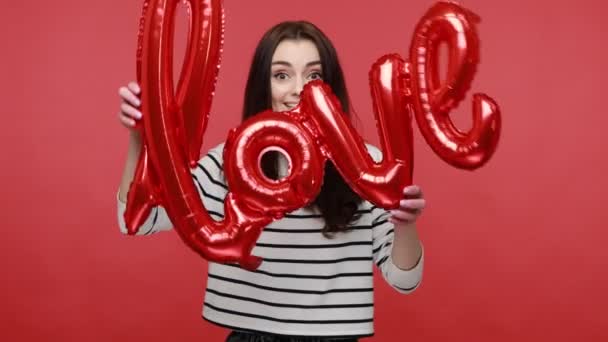 快乐的女人用锡箔球传递着爱的话语 表达着浪漫的感情 送出空气亲吻 穿着休闲风格的长袖衬衫 在红色背景下隔离的室内拍摄 — 图库视频影像