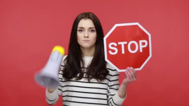 Ciddi esmer bir kadının portresi elinde kırmızı bir tabela ve megafon durağında uzun kollu bir gömlek giyerek çığlık atıyor. Kırmızı arkaplanda kapalı stüdyo çekimleri.