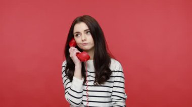 Öfkeli kadının portresi ev telefonu, iletişim, çatışma, uzun kollu sıradan bir gömlek giyerek yüksek sesle bağırıyor. Kırmızı arkaplanda kapalı stüdyo çekimleri.