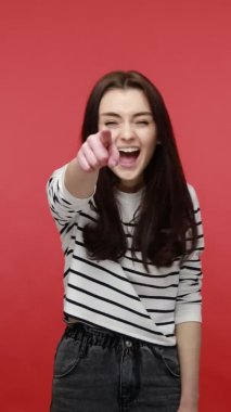 Pozitif kadının kamerayı işaret ettiği ve senden sesli bir şekilde güldüğü, seçim yaptığı, günlük tarz uzun kollu gömlek giydiği dikey video görüntüleri. Kırmızı arkaplanda kapalı stüdyo çekimleri.