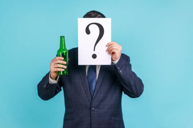 Portrait of anonymous person wearing dark official style suit hiding behind paper with question mark and holding bottle with alcohol. Indoor studio shot isolated on blue background. clipart