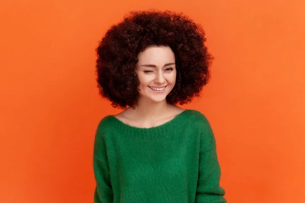 有非洲式发型的女人 穿着绿色休闲装 站着嬉笑着眨眼 表情积极 在橙色背景下被隔离的室内拍摄 — 图库照片