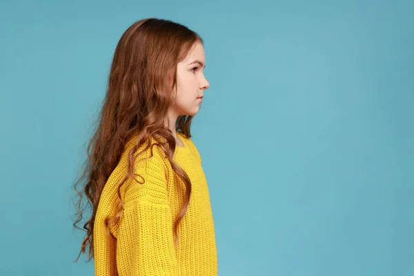 真っすぐ先を見て 黄色のカジュアルなスタイルのセーターを着て暗い波状の髪を持つ深刻なスマートボッシーの少女のサイドビューの肖像画 青い背景に隔離された屋内スタジオショット — ストック写真