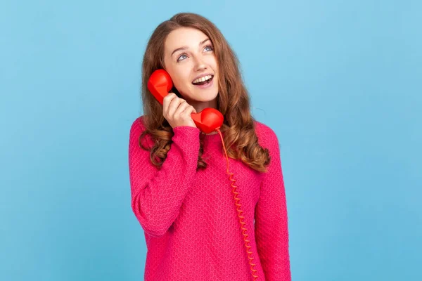 穿着粉色套头毛衣的快乐微笑的女人的画像 手里拿着红色复古电话 带着梦幻的表情望着远方 室内拍摄被蓝色背景隔离 — 图库照片