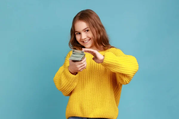 豊かな幸せな女の子お金を投げるの肖像画は カメラで笑みを浮かべて 肯定的な表現 黄色のカジュアルなスタイルのセーターを着ている 青い背景に隔離された屋内スタジオショット — ストック写真