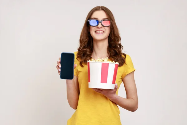 Obraz Pięknej Młodej Kobiety Trzymającej Popcorn Wiadrze Pokazujący Smartfona Pustym — Zdjęcie stockowe