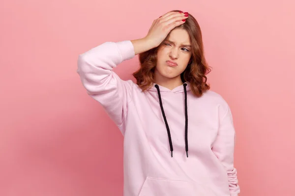 カジュアルパーカーの若い女性の損失の肖像悪い感情と頭に触れると 問題を心配立っている ピンクの背景に隔離された屋内スタジオショット — ストック写真