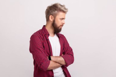 Depresif, sakallı, kırmızı gömlekli, kollarını kavuşturup bakan melankolik depresyonlu genç bir erkek portresi. Gri arka planda izole edilmiş kapalı stüdyo görüntüleri