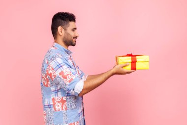 Yan manzara, mavi gömlekli neşeli sakallı adam hediyesini tutuyor, hediye kutusuna mutlu yıllar diliyor, yıldönümünü kutluyor. Pembe arka planda kapalı stüdyo çekimleri.