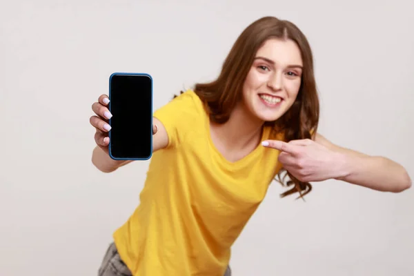 셔츠를 소녀가 핸드폰을 겨누며 카메라 앞에서 웃으며 물건을 추천하는 모습이다 — 스톡 사진