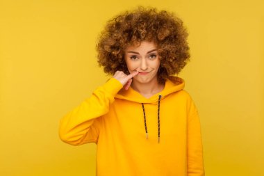 Afro saç stili şüphesi olan komik, kurnaz bir kadın. Fantezi kuran, plan yapan, şeytani şakalar planlayan, günlük tarz kapüşonlu bir şey giyen. Sarı arka planda kapalı stüdyo çekimleri.