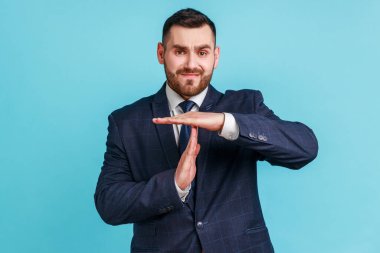 Daha fazla zamana ihtiyacım var! Koyu takım elbiseli, hayal kırıklığına uğramış esmer bir adamın portresi. Mola veriyor, kameraya bakıyor, son teslim tarihine yetişmek için acele ediyor. Mavi arka planda kapalı stüdyo çekimi.