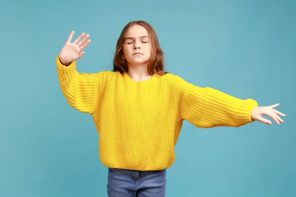 かわいい女の子の肖像目を閉じて 手を伸ばし 検索方法では 黄色のカジュアルなスタイルのセーターを着て歩く 青い背景に隔離された屋内スタジオショット — ストック写真