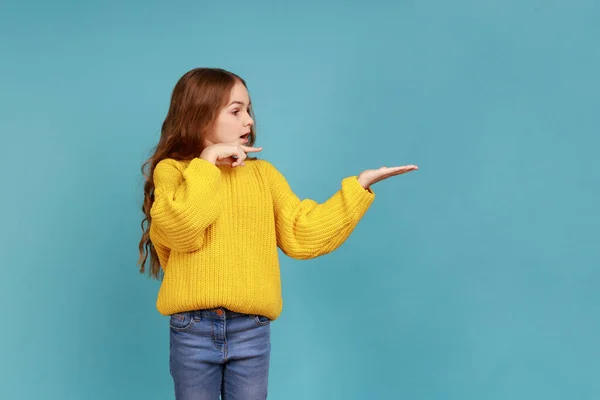 自由空間を提示する少女の肖像画 脇のポイント 広告のためのコピースペース プロモーション 黄色のカジュアルなスタイルのセーターを着て 青い背景に隔離された屋内スタジオショット — ストック写真