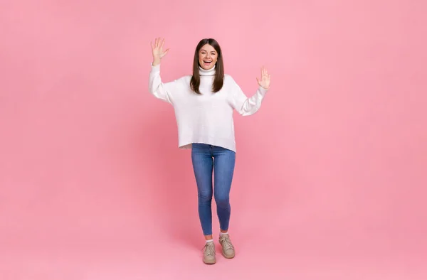 幸せな女性の完全な長さの肖像画のカメラに手を振って 良い気分が 白いカジュアルなスタイルのセーターを着て彼女の友人を迎える ピンクの背景に隔離された屋内スタジオショット — ストック写真