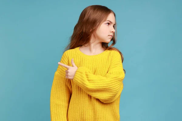 女の子の肖像画の出口を示すことを指摘し 彼女だけを残して 憤慨感を求めて 黄色のカジュアルなスタイルのセーターを着て 青い背景に隔離された屋内スタジオショット — ストック写真