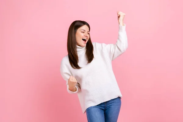 白いカジュアルなスタイルのセーターを着て 勝利と彼女の成功を祝う 洗練された拳で立って幸せな興奮した女性の肖像画 ピンクの背景に隔離された屋内スタジオショット — ストック写真