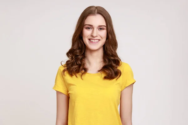 黄色のカジュアルなTシャツの明るいティーンエイジャーの少女の肖像画を誠実にカメラでは 肯定的な気分笑みを浮かべて 誰かを満たすために喜んでいる 灰色の背景に隔離された屋内スタジオショット — ストック写真