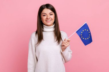 Çekici, siyah saçlı, elinde Avrupa sendikası bayrağını tutan ve kameraya gülümseyen beyaz, sıradan bir süveter giyen bir kadın. Pembe arka planda kapalı stüdyo çekimleri.