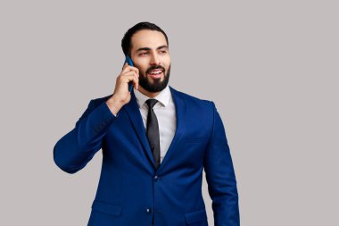 Gülümseyen adam, akıllı telefon konuşuyor, telefon ediyor ve resmi tarz takım elbise giymiş, iş ortağı veya arkadaşıyla hoş sohbetler ediyor. Gri arka planda izole edilmiş kapalı stüdyo görüntüleri.