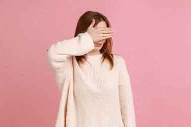 Utanç portresi, kafası karışık sarışın kadının gözlerini kapayarak gözlerini kapatması, saklanması, görmezden gelmesi görmek istememesi beyaz kazak giymesi. Pembe arka planda kapalı stüdyo çekimleri.