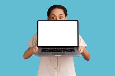 Yüzünün yarısını laptopla kaplayan rastalı kadın portresi reklam ya da tanıtım metni için boş bir ekran, gömlek giyiyor. Mavi arka planda kapalı stüdyo çekimi.