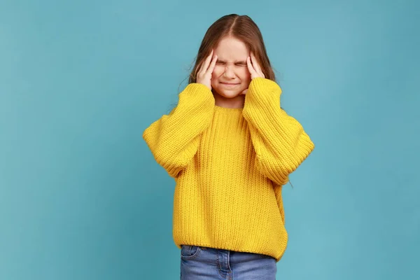 小さな女の子の寺院の激しい頭痛 子供片頭痛 医療問題に苦しんで 黄色のカジュアルなスタイルのセーターを着て感じてクラッチ 青い背景に隔離された屋内スタジオショット — ストック写真