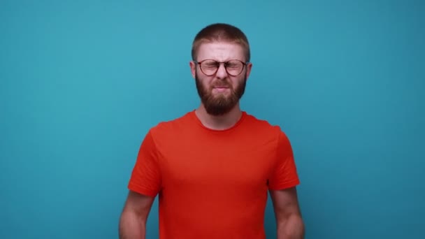 橙色胡子的男人用手指揉揉眼睛 眼镜下疲惫的眼睛长时间工作 过度劳累 穿着橙色T恤 室内拍摄被蓝色背景隔离 — 图库视频影像