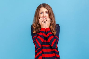 Sorunlar ve endişeler. Çizgili kazak giyen, tırnaklarını yiyen, sorunlardan korkan, fobisi olan, anksiyete bozukluğu çeken gergin bir kadının portresi. Mavi arka planda kapalı stüdyo çekimi.
