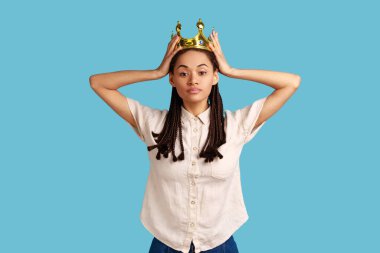 Altın taçlı siyah rastalı hırslı bir kadın kendini göstererek küstahça, otoritesini ilan ederek, üstün ayrıcalıklı statüsünü ilan ediyor. Mavi arka planda kapalı stüdyo çekimi.