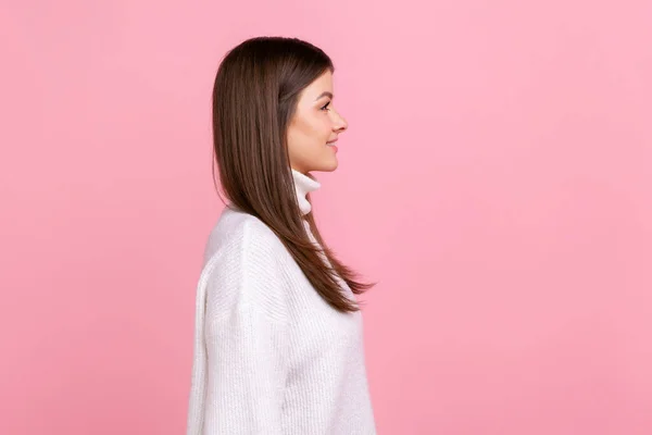 笑顔のブルネットの女性のサイドビューの肖像画は 幸福を表現し 良い気分にされ 白いカジュアルなスタイルのセーターを着て先に見えます ピンクの背景に隔離された屋内スタジオショット — ストック写真