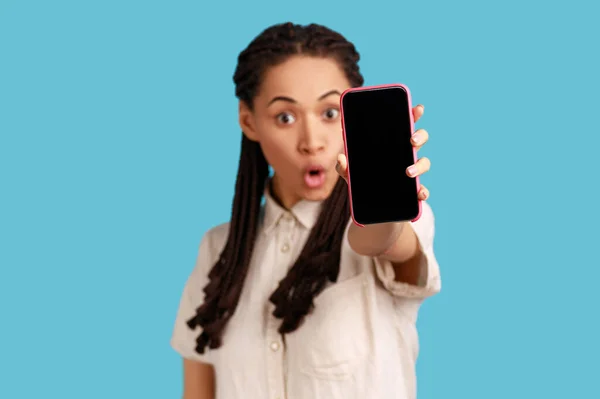 更新此应用程序 令人惊讶的迷人女人 黑色的可怕的头发伸出了手机 震惊于它的功能 互动的移动界面 室内拍摄被蓝色背景隔离 — 图库照片