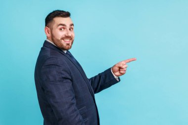 Vay canına, şu reklamlara bak! Resmi stil takım elbise giyen sakallı iş adamının yan görünüşü fikir sunumu için boş fotokopi alanı gösteriyor. Mavi arka planda kapalı stüdyo çekimi.