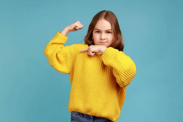 小さな女の子の肖像画の両足を指して 強力で自信を持って 強さを示し 黄色のカジュアルなスタイルのセーターを着て感じている 青い背景に隔離された屋内スタジオショット — ストック写真