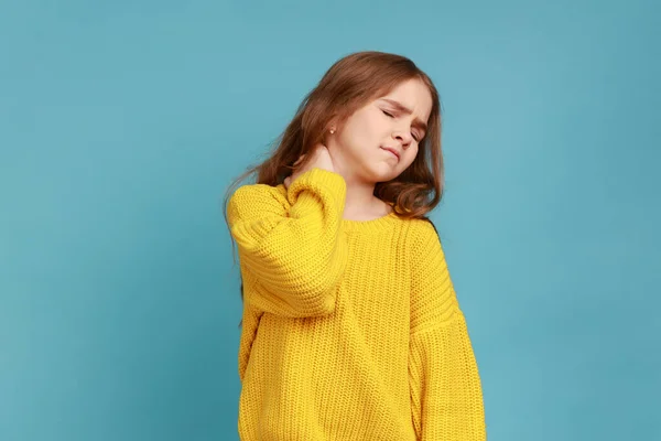 少女の肖像画に戻る痛みを伴うマッサージ 首の不快感を感じる 子供の鎮静剤のライフスタイル 黄色のカジュアルなスタイルのセーターを着て 青い背景に隔離された屋内スタジオショット — ストック写真