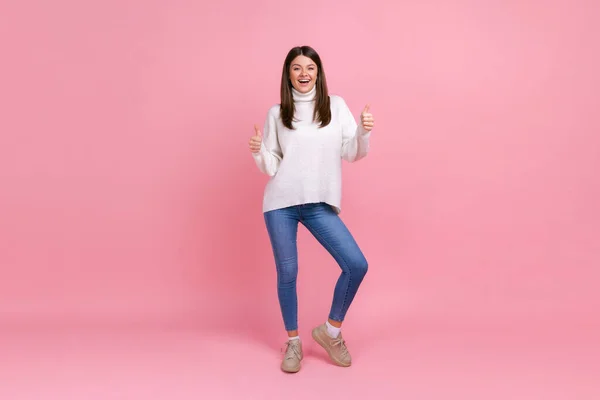 幸せな笑顔楽観的なブルネットの女の子の完全な長さの肖像画親指を表示し ジェスチャーを承認し 白いカジュアルなスタイルのセーターを着ています ピンクの背景に隔離された屋内スタジオショット — ストック写真