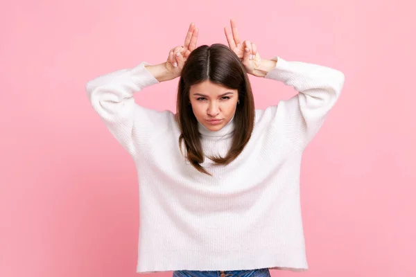 積極的な女性の頭の角 傲慢と頑固な 攻撃する準備ができて 白いカジュアルなスタイルのセーターを着て上の指を保持 ピンクの背景に隔離された屋内スタジオショット — ストック写真