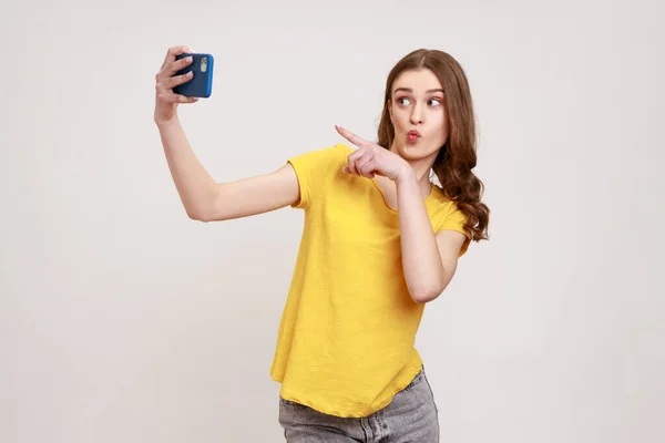 Amistosa Adolescente Con Camiseta Amarilla Apuntando Con Dedo Teléfono Celular —  Fotos de Stock