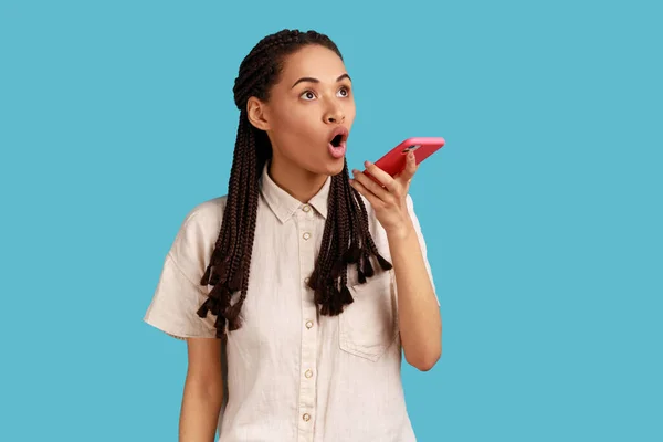 令人惊讶的情绪激动的黑发女人在现代手机上使用语音识别应用程序 记录信息 穿着白衬衫 室内拍摄被蓝色背景隔离 — 图库照片